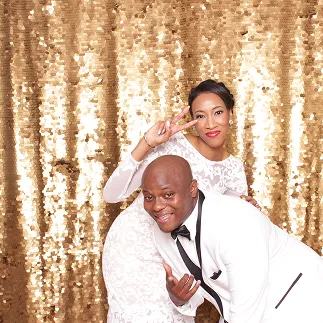 Couple posing at a gold-sequin photo booth backdrop