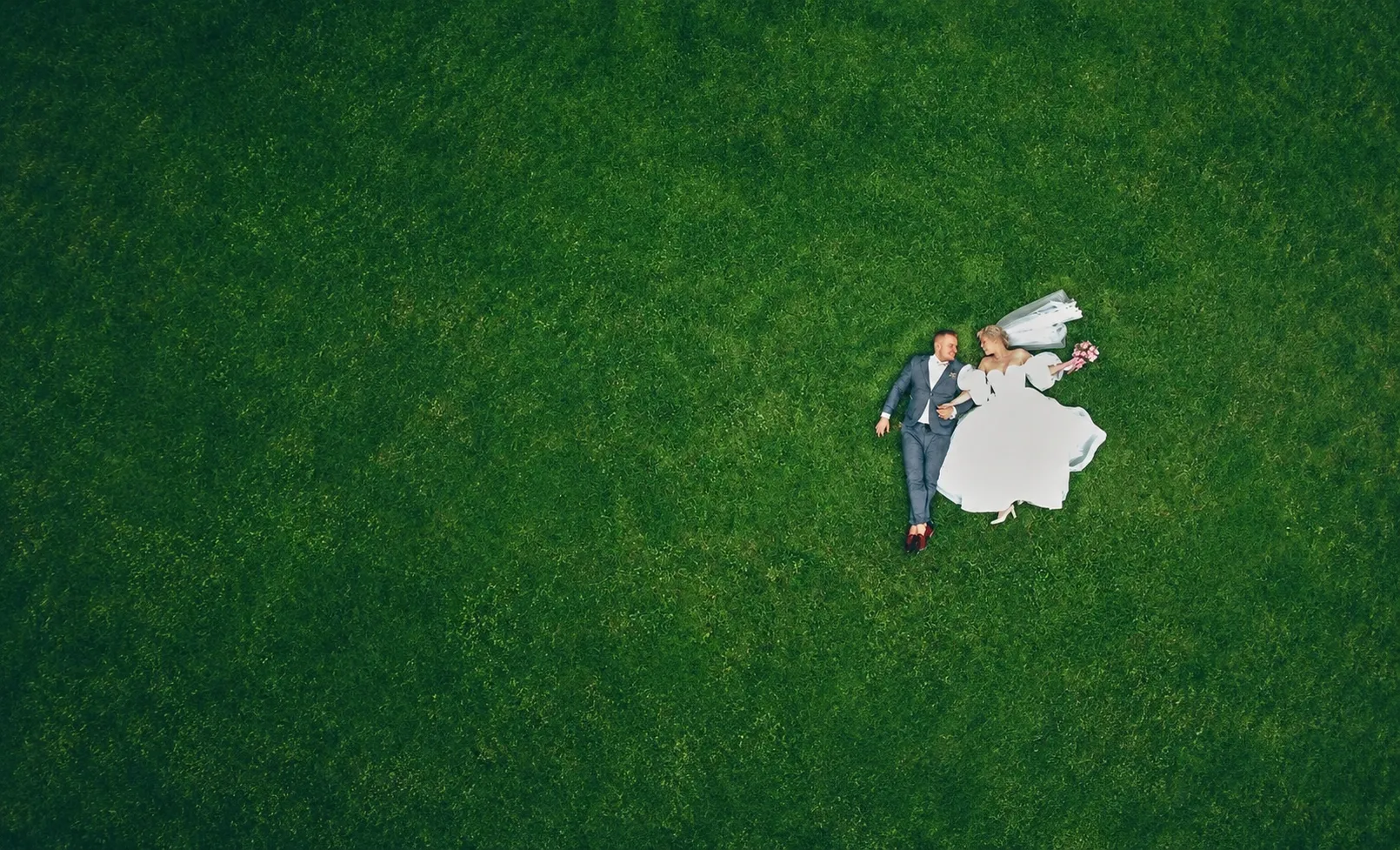 Aerial drone photograph of a wedding couple lying on a green lawn